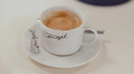 Weiße Cappuccino-Tasse mit Aufschrift „Autohaus Engel“ auf passender Untertasse, gefüllt mit Kaffee.