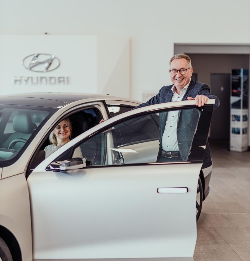 Hyundai-Verkäufer öffnet einer Kundin die Autotür für ein Probesitzen im Showroom