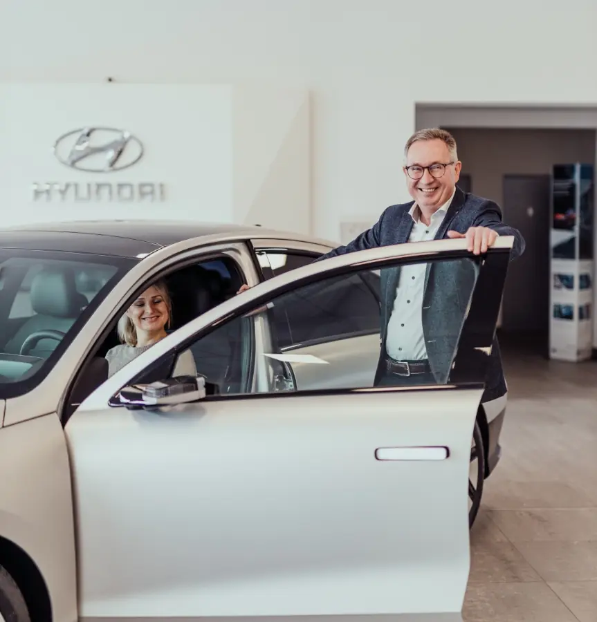 Hyundai-Verkäufer öffnet einer Kundin die Autotür für ein Probesitzen im Showroom