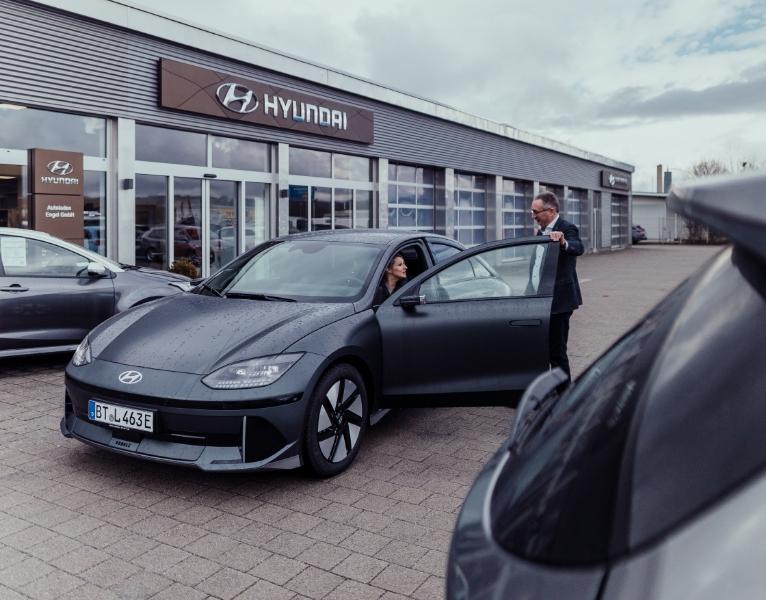 Hyundai IONIQ 6 vor dem Autohaus Engel, Verkäufer öffnet einer Kundin die Fahrertür zur Probefahrt