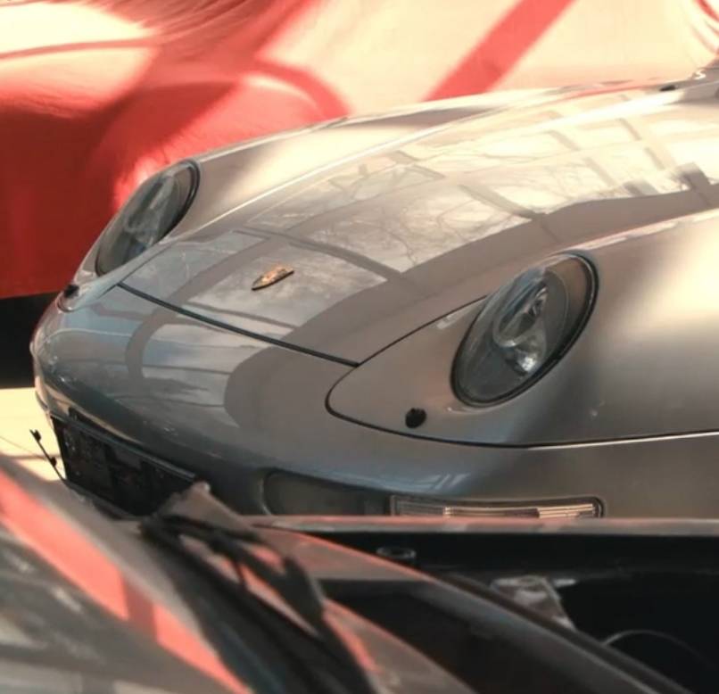 Frontansicht eines silbernen Porsche 911 Oldtimers mit runden Scheinwerfern und Porsche-Wappen auf der Motorhaube.